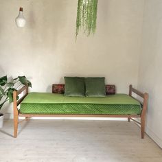 a green daybed in a white room next to a potted plant