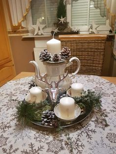 a table topped with white candles and pine cones on top of a plate covered in greenery