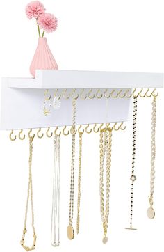 a white shelf with lots of necklaces hanging from it's sides and a pink flower in a vase on top