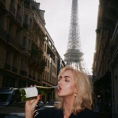 a woman drinking from a bottle in front of the eiffel tower, paris