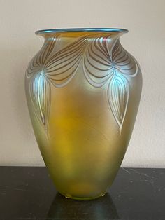 a large glass vase sitting on top of a black table next to a white wall