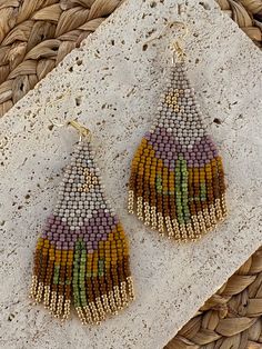 a pair of beaded earrings sitting on top of a white stone slab next to a woven basket