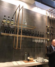 a man standing in front of a wine rack filled with bottles and glasses on top of a counter