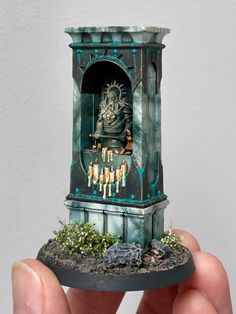 a miniature clock tower in the palm of someone's hand, with candles on it