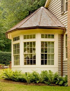 a white gazebo sitting in the middle of a lush green yard next to a brick building