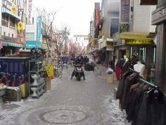 a man riding a motorcycle down a street next to shops and businesses in the snow