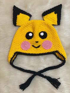 a crocheted yellow hat with black ears and pink eyes is laying on a white fur surface