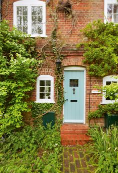 a blue door in front of a brick building with white windows and green plants around it