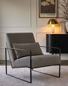 a gray chair sitting on top of a white rug next to a black table and lamp