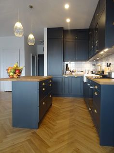 a kitchen with wooden floors and blue cabinets in the center is lit by pendant lights