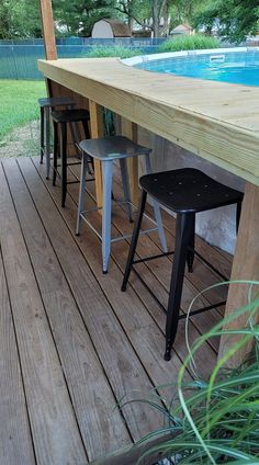 an outdoor bar with stools next to a swimming pool and wooden decking area