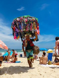 a man walking on the beach carrying an umbrella over his head with other people in the background