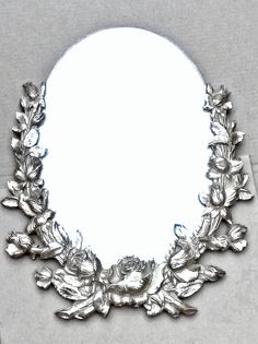 a mirror that has some silver flowers on the edge and leaves in front of it