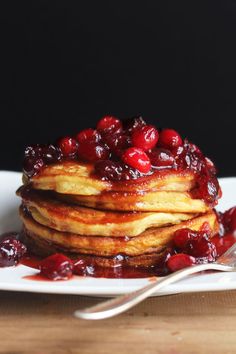 a stack of pancakes with cranberries on top and syrup drizzled over them