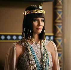 an egyptian woman wearing gold jewelry and pearls on her head, standing in front of a wall