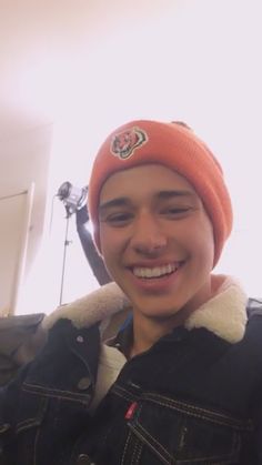 a young man wearing an orange beanie smiles at the camera