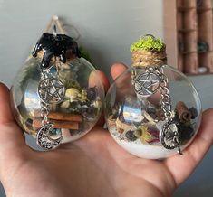 two clear glass ornaments with various items in them, one being held by a hand