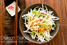 a bowl filled with salad next to chopsticks on top of a wooden table