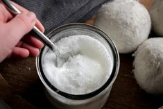 a person spooning sugar into a jar filled with doughnuts on top of a wooden table