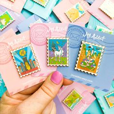 a person holding three different colored stamps on top of pink and blue envelopes in front of them