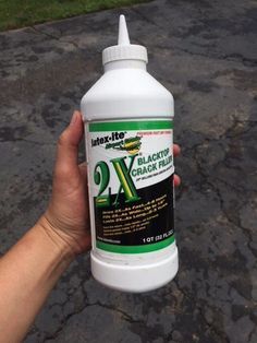 a hand holding a gallon of blacktop oak rubr on the pavement with grass in the background