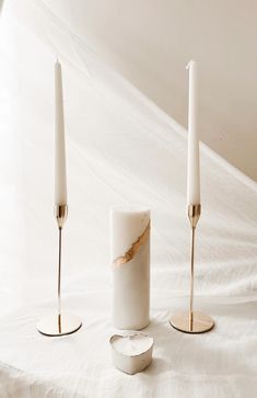 three white candles sitting on top of a bed next to each other