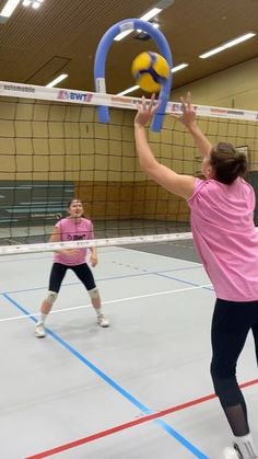 two women playing volleyball on an indoor court with one blocking the ball and the other blocking the net