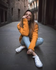 a young woman sitting on the ground in an alleyway with her hand to her face