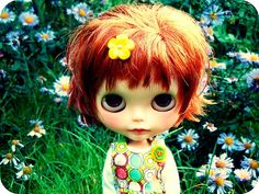 a close up of a doll with red hair in a field of flowers and daisies