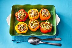 several stuffed peppers on a green plate with a spoon and fork next to the tray