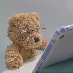 a brown teddy bear wearing glasses sitting next to a tablet