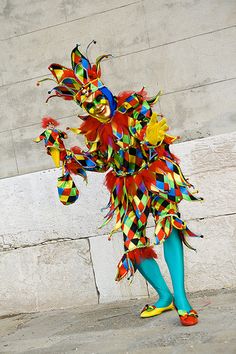 a woman dressed in brightly colored clothing standing next to a wall