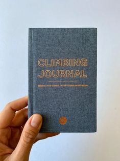 a person holding up a book with the title climbing journal written in gold on it