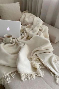 an apple laptop sitting on top of a bed covered in white blankets and throw pillows