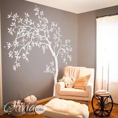 a living room with a tree painted on the wall and white furniture in front of it