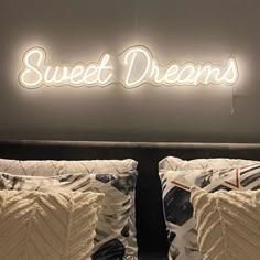 two white pillows sitting on top of a bed under a neon sign that says sweet dreams