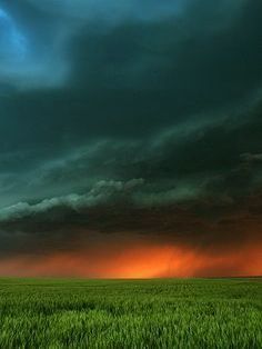 the sky is very dark and cloudy over an open field with green grass in front of it