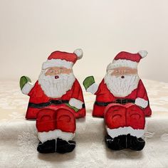 two santa clause figurines sitting on top of a white cloth covered tablecloth