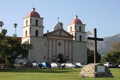 an old church with two towers and a cross on the lawn in front of it