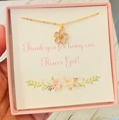 a hand holding a pink box with a gold flower charm on it's chain