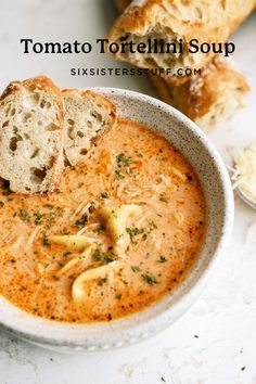 a bowl of tomato tortellini soup with two pieces of bread on the side