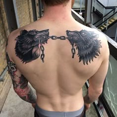 a man with tattoos on his back is chained to two wolf heads