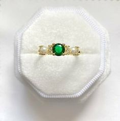 an emerald and pearl ring sits on a white cloth