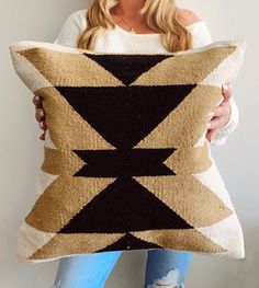 a woman holding a black and tan pillow with an arrow design on it, in front of a white wall