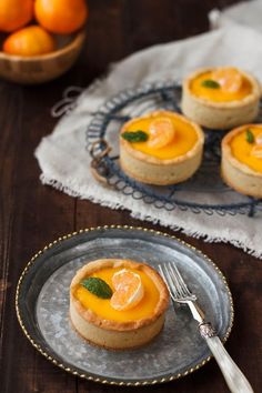 small tarts with oranges in the background on a plate and a fork next to them