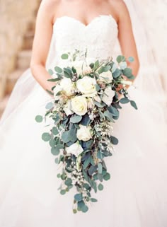 a bride holding a bouquet of white flowers and greenery in her wedding day dress