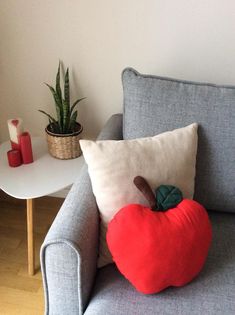 a heart shaped pillow sitting on top of a gray couch next to a potted plant