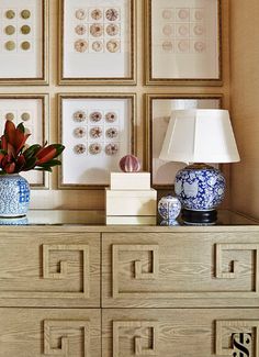 a wooden dresser topped with blue and white vases next to pictures on the wall