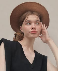 a woman wearing a brown hat and black dress posing for the camera with her hand on her face