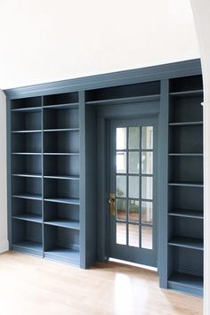 an empty room with blue bookshelves and wooden flooring in front of the door